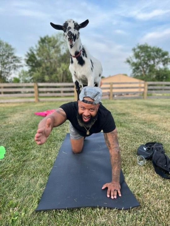 Hemory posing with a goat on his back while doing yoga.